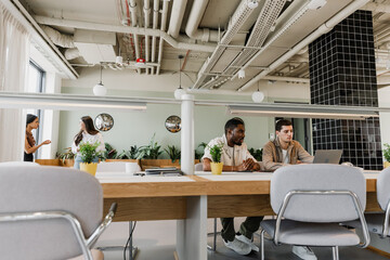 Two male workers looking at a laptop and sitting at a table while one of them talks