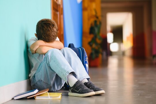 Upset boy sitting at school and crying after bullying by pupils classmates