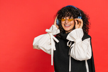 Caucasian young woman with curly hair listening music on headphones, dancing disco fooling around...