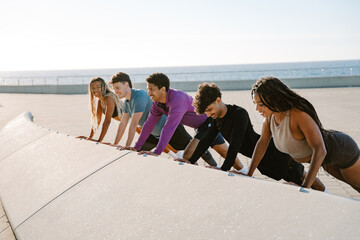 A group of five athletes are smiling and leaning on their hands while standing in a push-up position