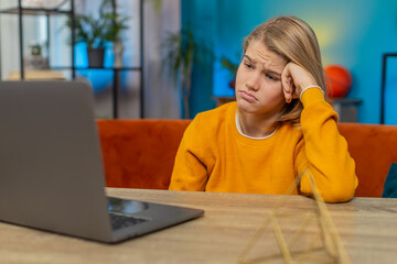 Caucasian teenager boy receiving bad news on laptop at home. Seeing poor education exam results negative grades at school, sitting gloomily on couch by table, looking at screen with sad expression
