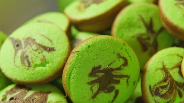 A close-up video of delicious Indonesian green pandan cakes (kue cubit). The small, round snacks have a beautiful chocolate marble swirl. A warm and authentic food scene.

