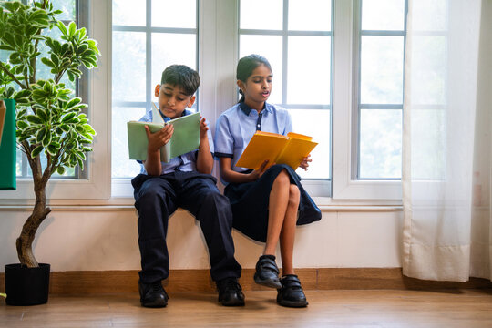 Indian Uniformed students quietly read near classroom window during peaceful self-study time - Powered by Adobe