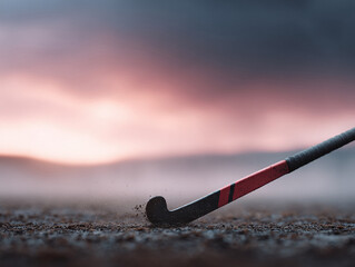 Dramatic action shot of a field hockey stick hitting the ground, dust flying. Sunset sky. Represents determination, sportsmanship, and athletic passion. Great for sportsthemed content