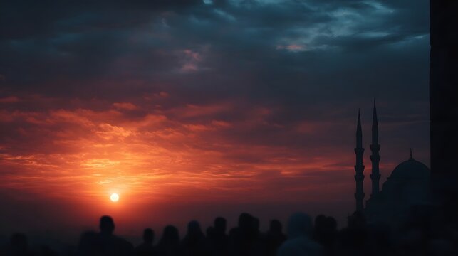 A breathtaking sunset paints the sky in vibrant hues of orange and red above a silhouetted mosque as a crowd of worshippers gathers in the fading