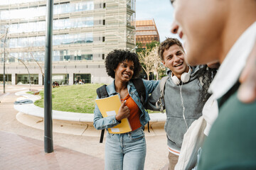 A female student is holding a notebook and hugging a male student who is talking while they are laughing and standing next to two students