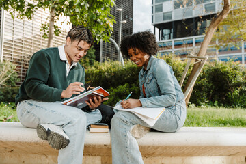 Male and female students sitting and smiling while she writes in a notebook and he reads