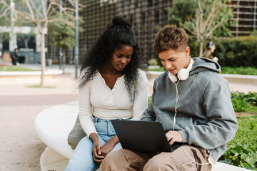 A male student is typing on a laptop as a female student sitting next to him looks at it