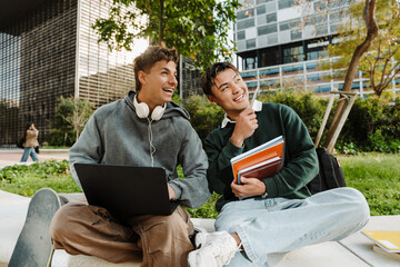 Two male students sit and laugh while looking in the direction one of them is pointing with a pen...