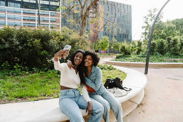 Naklejka premium A female student hugs a female student sitting next to her while they smile and pose in front of a phone that one of them is holding
