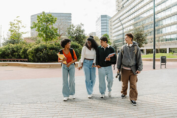 A group of four friends are walking and laughing while three of them look at the other