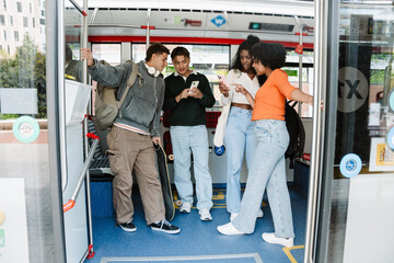 A group of four students talk and in pairs look at the phones that two of them are showing while...