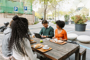 A group of four students sit at a table while one of them types on a laptop