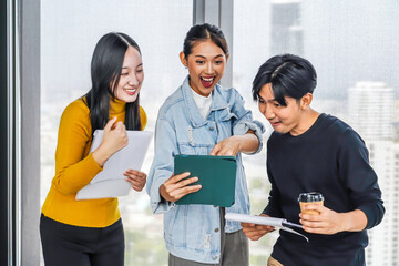 Asian business team professionals in an office setting joyfully celebrates their recent...