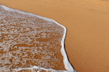 Gentle ocean wave washing over golden sand at the beach. The soft foam and clean shoreline capture a calm, minimal summer scene symbolizing peace, nature, and seaside tranquility.