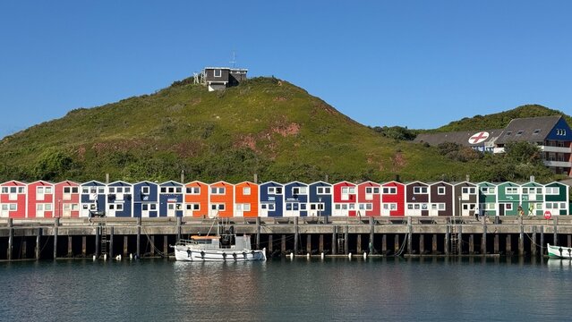 Blick vom Meer auf die Insel Helgoland mit bunten Hummerbuden unter blauem Himmel