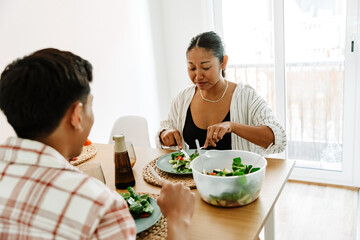 A woman is cutting a salad and listening to a man sitting across from her at the table
