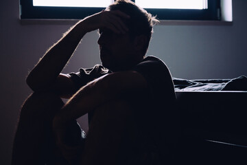 Silhouetted mature man sitting hopeless and depressed on bedroom floor, mental health and...