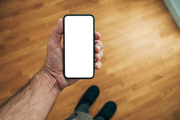 Male hand holding smartphone with blank screen in cozy living room, symbolizing digital connection, communication, and modern lifestyle.