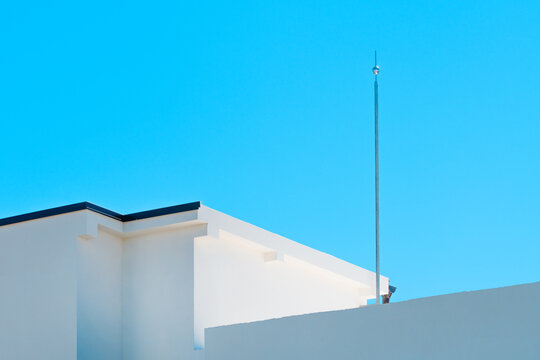 Lightning rod mounted on top of a building against clear blue sky, symbol of safety and protection.