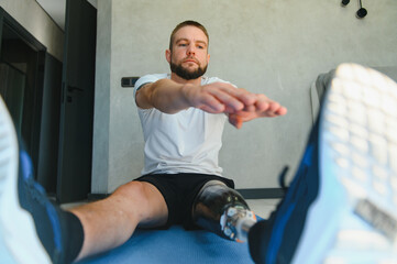 Man amputee with prosthetic leg disability on transfemoral leg prosthesis artificial device making stretching rehabilitation physical exercise at home. People w amputation disabilities everyday life