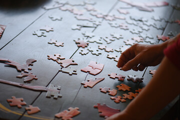 holding a puzzle piece in his hand, a disassembled puzzle on the table, a dark atmosphere.