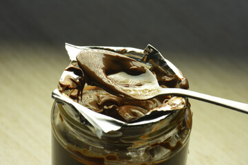 Chocolate cream, jar with spoon in liquid chocolate, cocoa cream close-up.