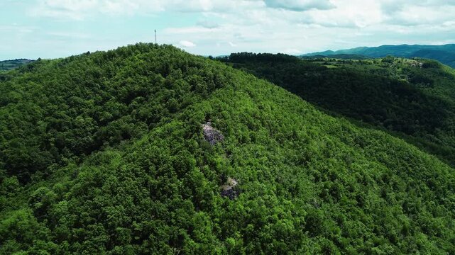 Drone view of Velika Stena viewpoint in Serbia, a rocky cliff surrounded by lush green forest and scenic hills. Horizontal 4k footage