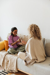 Daughter laughing and playing rock paper scissors with her mother while they sit on the couch