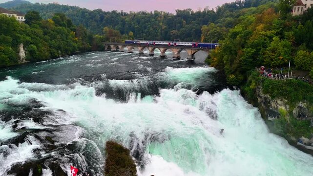 Aerial drone view of the Rheinfall, the largest and one of the most powerful waterfalls in Europe, located in Switzerland. A train passes by the waterfall. 