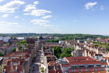 Aerial panoramic view of the historic Old Town of Gdańsk, Poland, with red tiled rooftops, bustling pedestrian street, and surrounding green landscape on a sunny summer day
