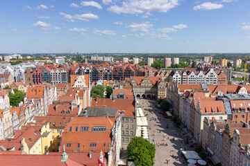 Aerial panoramic view of the historic Old Town of Gdask, Poland, with red tiled rooftops, bustling pedestrian street, and surrounding green landscape on a sunny summer day