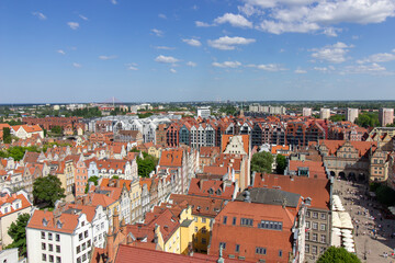 Aerial panoramic view of the historic Old Town of Gdask, Poland, with red tiled rooftops, bustling pedestrian street, and surrounding green landscape on a sunny summer day