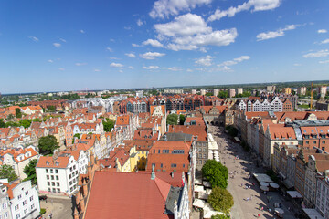Aerial panoramic view of the historic Old Town of Gdask, Poland, with red tiled rooftops, bustling pedestrian street, and surrounding green landscape on a sunny summer day