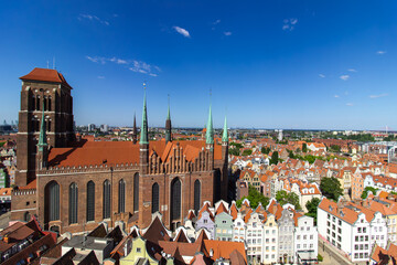 Aerial panoramic view of the historic Old Town of Gdask, Poland, with red tiled rooftops, bustling pedestrian street, and surrounding green landscape on a sunny summer day
