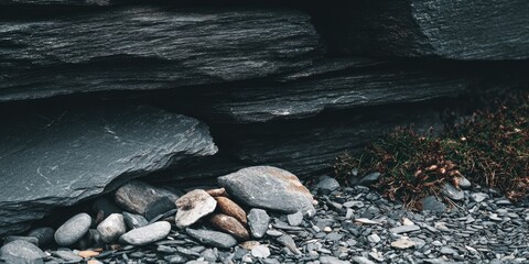Obraz premium Dark grey rocks and stones at the base of a cliff face. A small patch of moss or lichen is visible near the bottom right