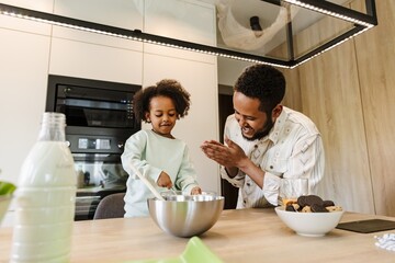 A father stands at the table and laughs while his daughter stirs in a bowl next to him