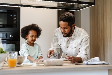 A father and his daughter are standing at the table and cooking