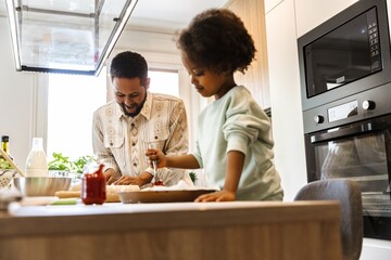 The daughter puts the sauce on the dish while her father stands next to her and laughs