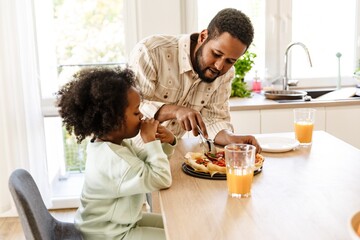 A father stands and cuts a pizza at a table where his daughter sits