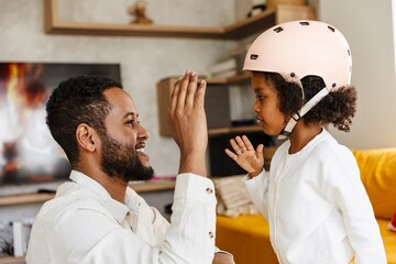 A father laughs as his daughter stands in front of him and they give each other a high five