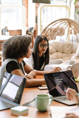 Two female workers are looking at a laptop that one of them is pointing at while sitting at the table