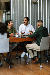 A group of three workers are talking and sitting at a table while two of them are smiling