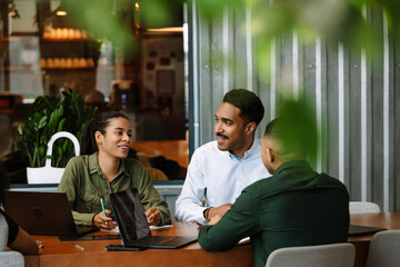 A group of three employees are sitting at a table and two of them are smiling while one of them is talking