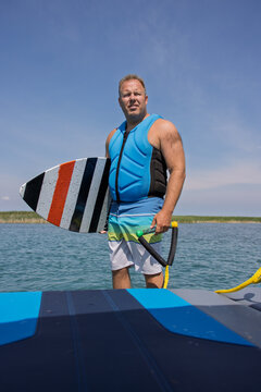 Man standing on a boat while holding a surfboard and rope