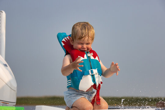 Child kneeling and gesturing on a boat and wearing a life jacket