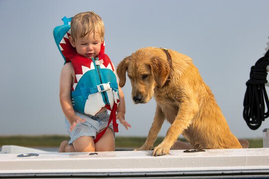 Child wearing a life jacket on a boat with his dog