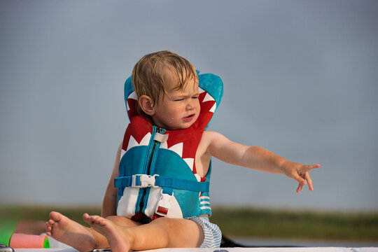 Child sitting and pointing while wearing a life jacket