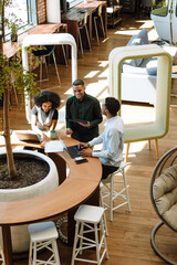 A male worker is holding a computer tablet and laughing while standing next to female and male...