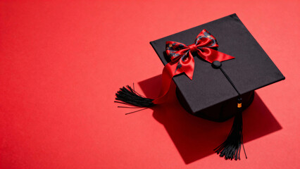 Black graduation cap with red bow on a red background